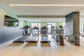 A gym with treadmills, elliptical machines, and a television.